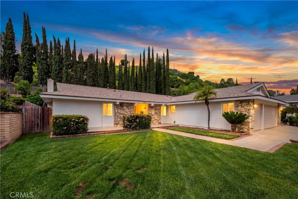 Single-story home with stone accents, a broad lawn, and tall cypress trees at sunset.