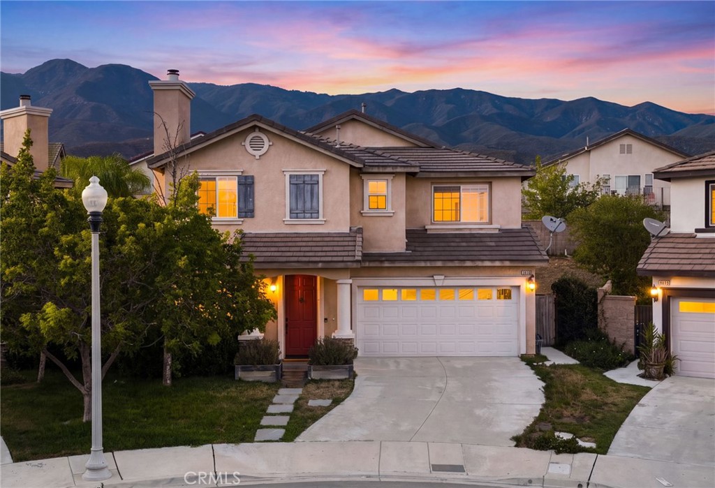 Two-story stucco home with lit windows, a red front door, and mountains behind it at dusk.