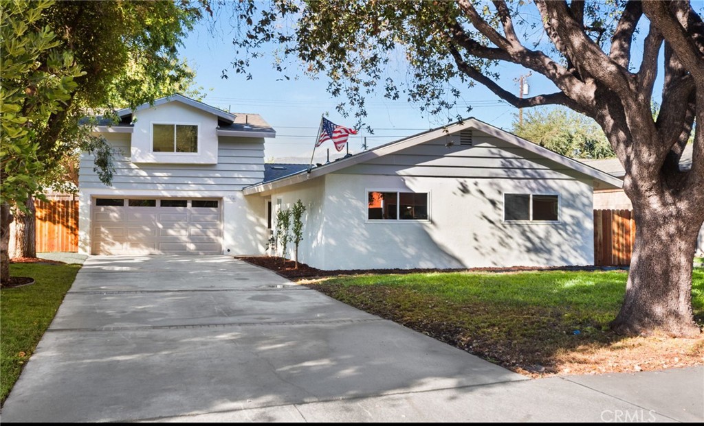 White California home with a broad driveway, prominent garage, mature trees, and an American flag.