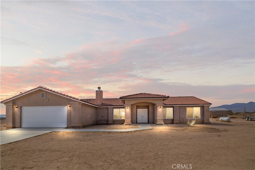 Single-story stucco home with a two-car garage on a bare lot at sunset.