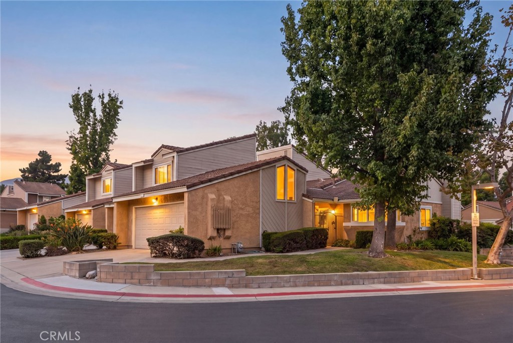 Two-story suburban home with a garage and mature trees, its windows glowing at dusk.