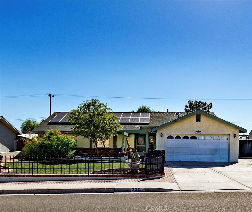 Single-story house with rooftop solar panels, a two-car garage, and a fenced landscaped front yard.