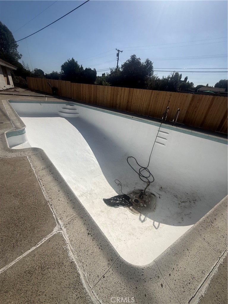 Drained in-ground pool with a white interior, curved steps, and repair equipment on the floor.