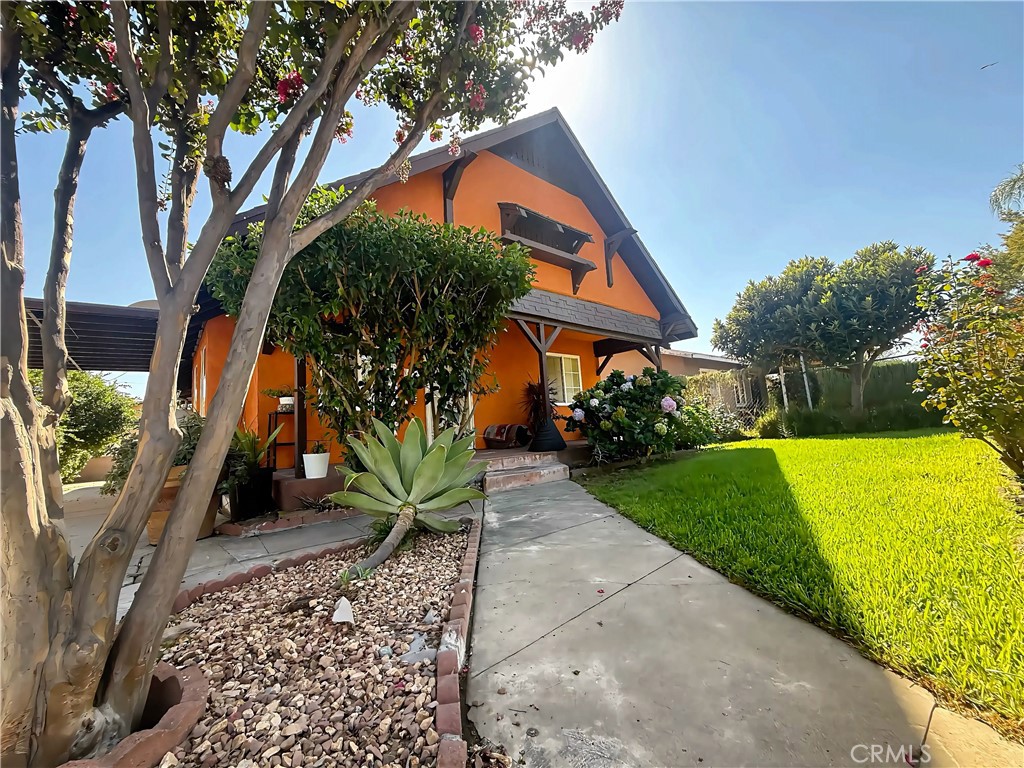 Orange two-story house with dark trim, shaded porch, mature trees, and a landscaped front yard.
