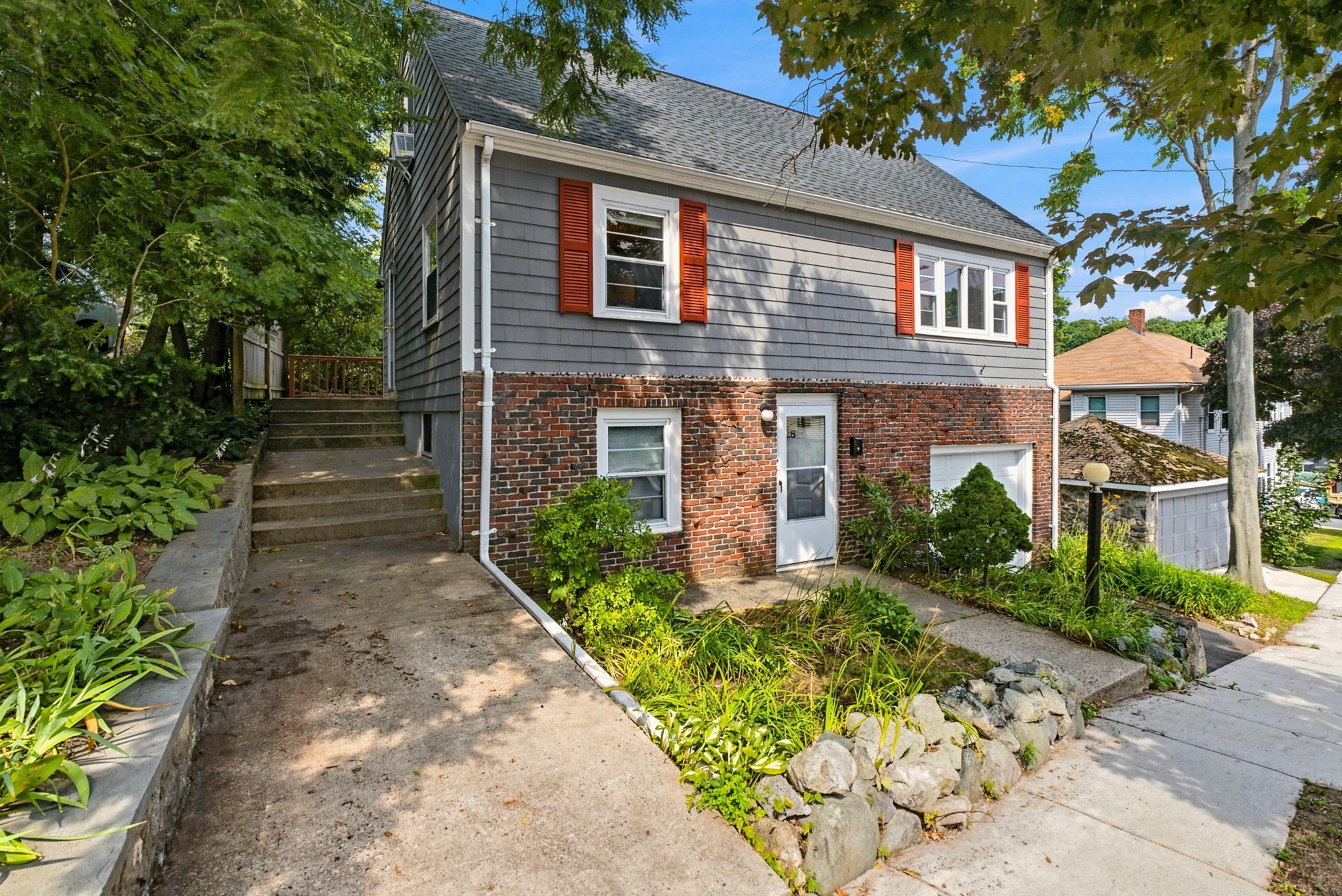 Gray-sided house with a brick lower level, orange shutters, and landscaped entry paths.
