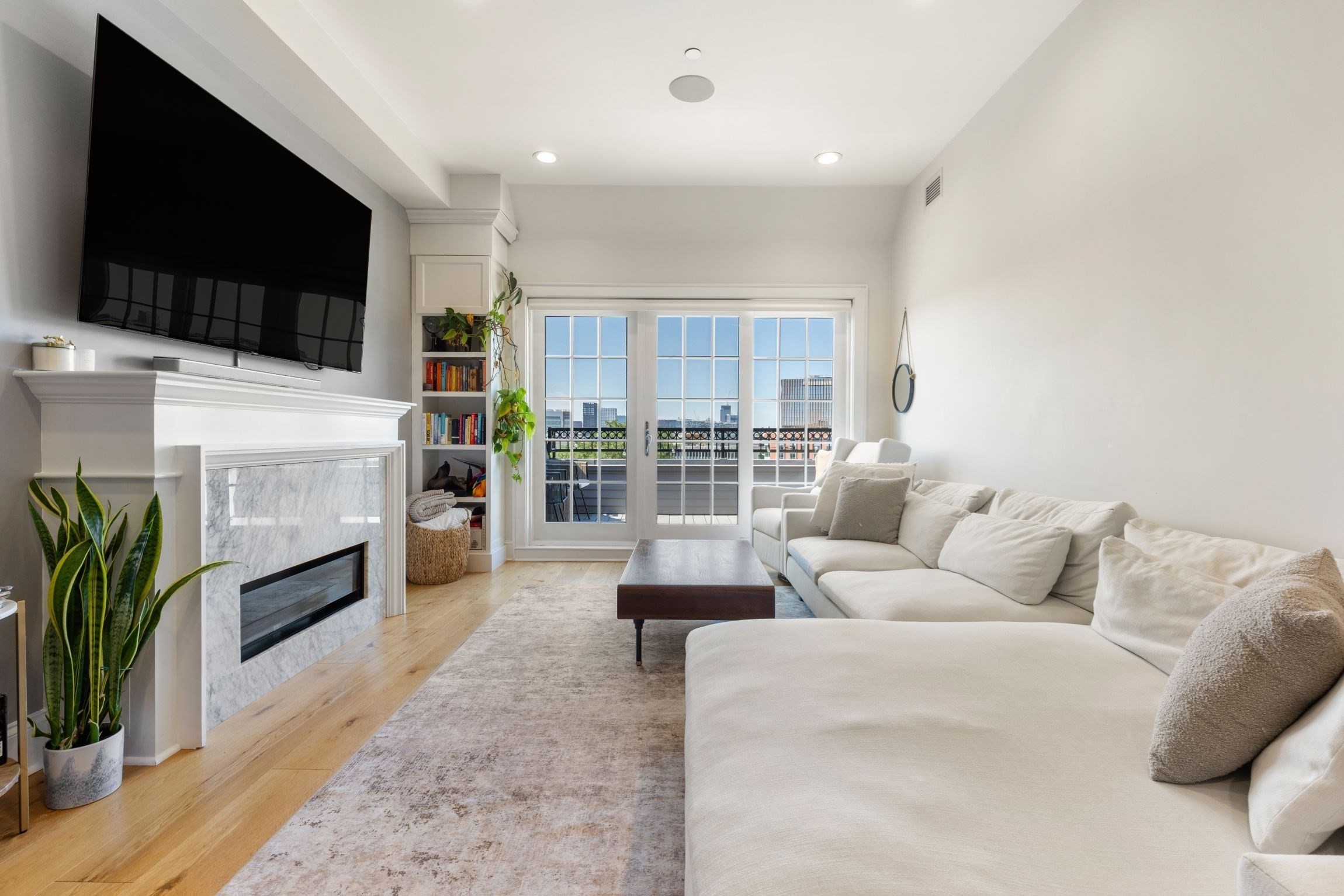 Living room with a white sectional, marble fireplace, and French doors opening to a city-view balcony.
