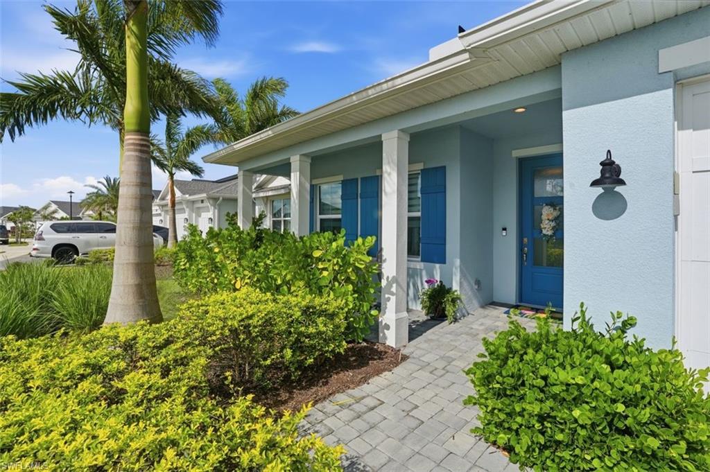 Light-blue home with a blue front door, covered porch, paved walkway, and palm-lined landscaping.