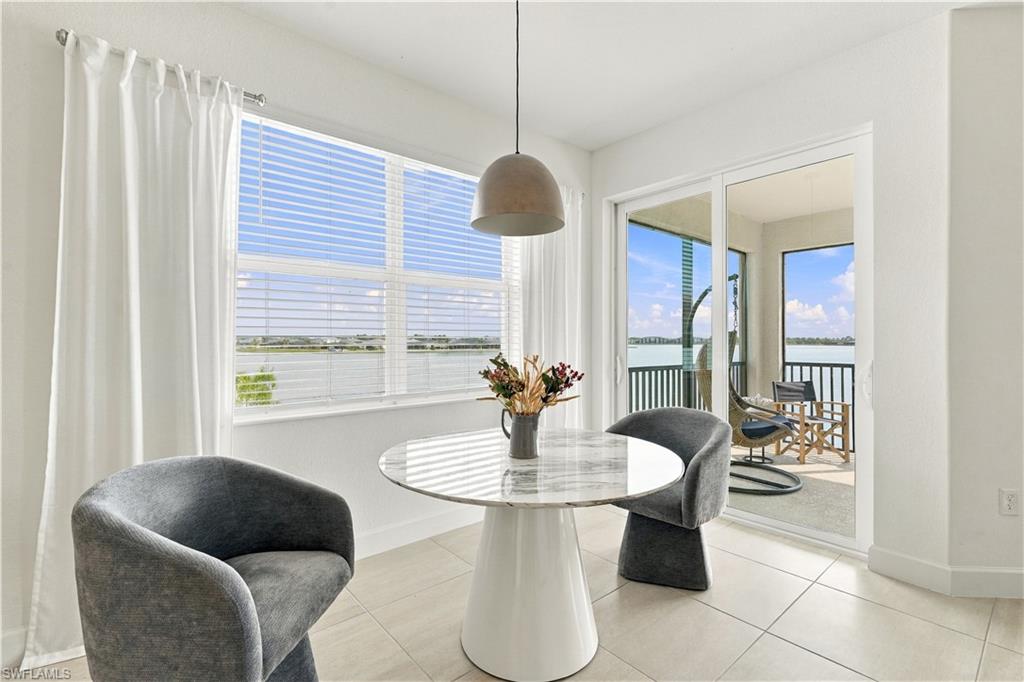 Dining area with a round pedestal table and gray chairs overlooking the water from a balcony.