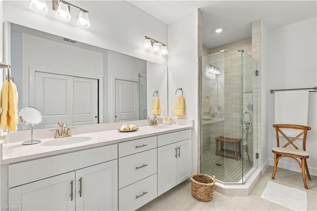 Bathroom with a long white vanity and glass-enclosed tiled shower.