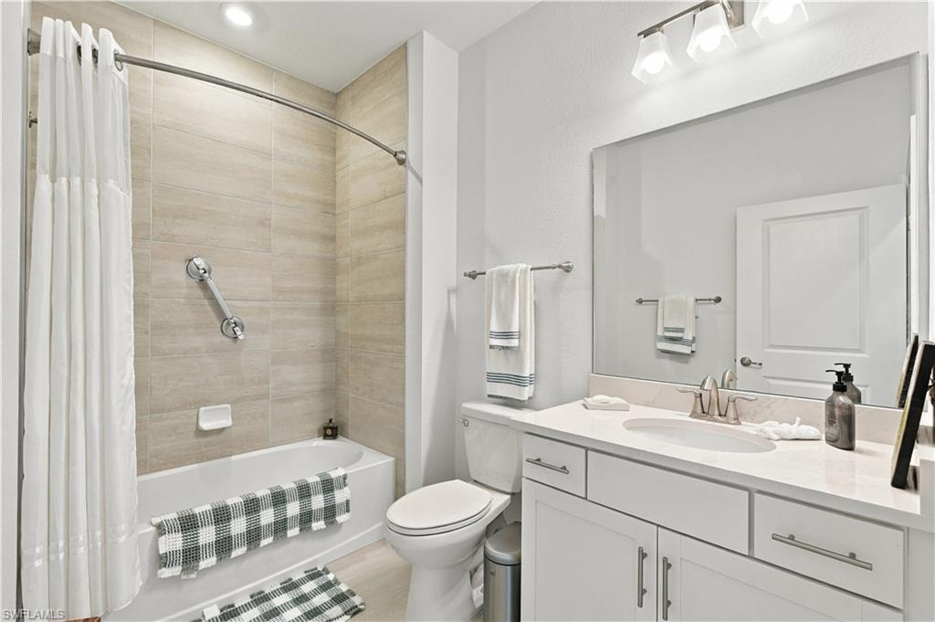 Bathroom with a tiled tub-shower, white vanity, large mirror, and striped towels.