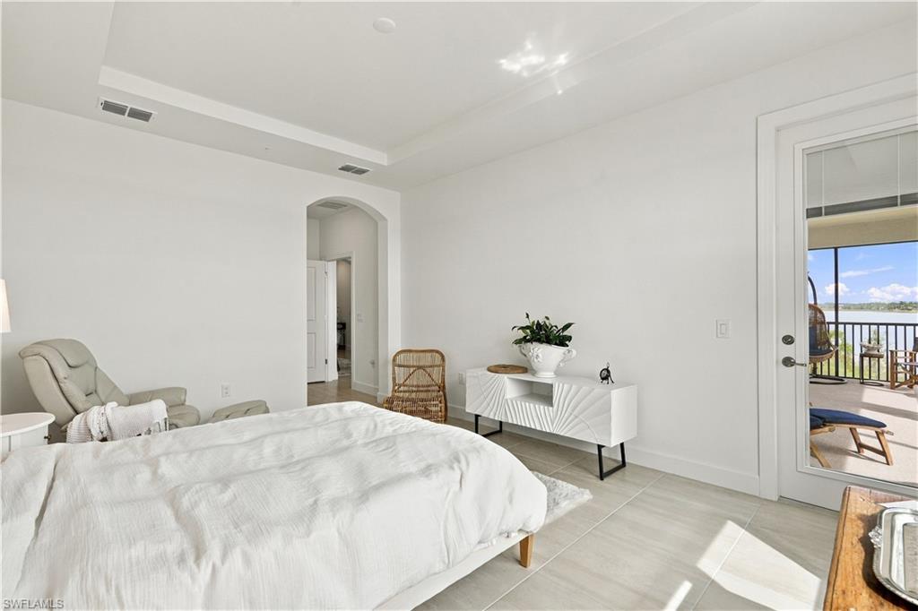 Bright bedroom with a white bed and glass door opening onto a water-view balcony.