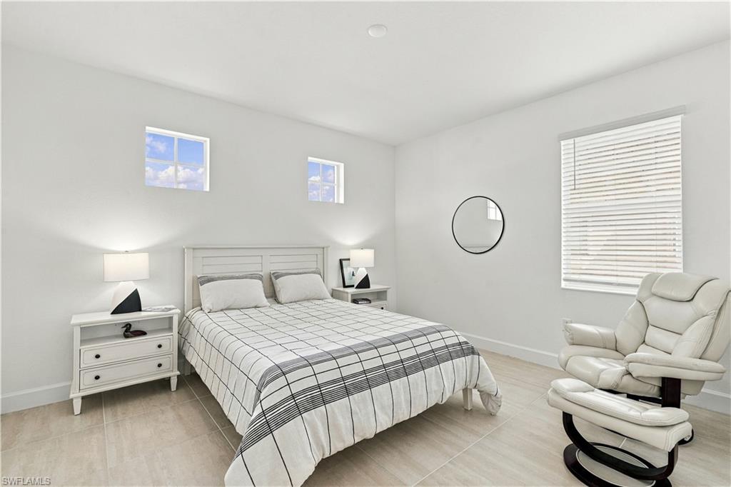 Bedroom with a white bed, two high windows, and a white leather recliner.