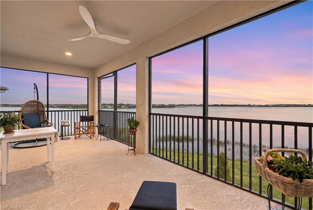 Covered balcony overlooking calm water at sunset, with large windows and seating.