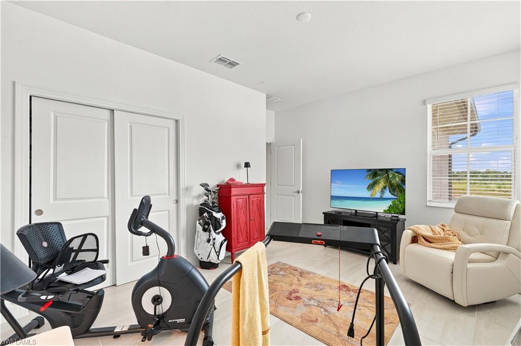 Bright exercise room with stationary bikes, golf clubs, television, and a cream recliner.