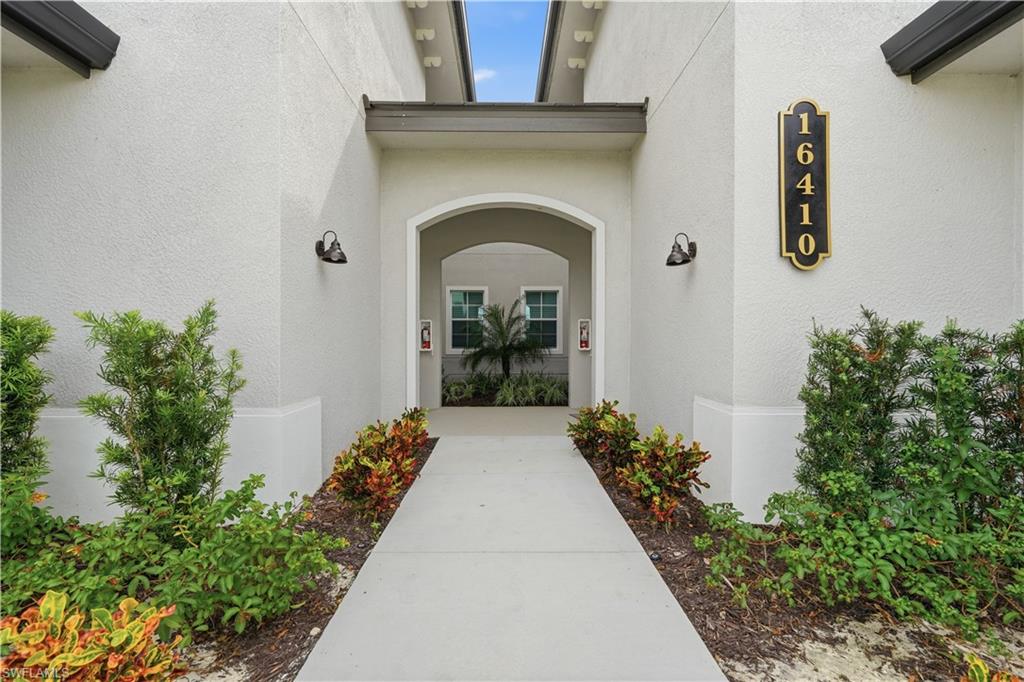 Stucco property entrance with an arched doorway, landscaped walkway, and vertical 16410 plaque.