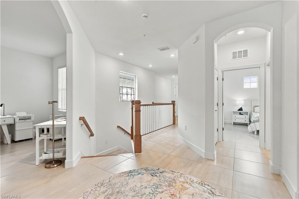 Upstairs hallway with tiled floors, a wood-and-white stair railing, and a bedroom visible through an arched doorway.