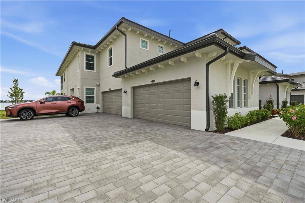 Two-story stucco house with two garage doors and a wide paver driveway.