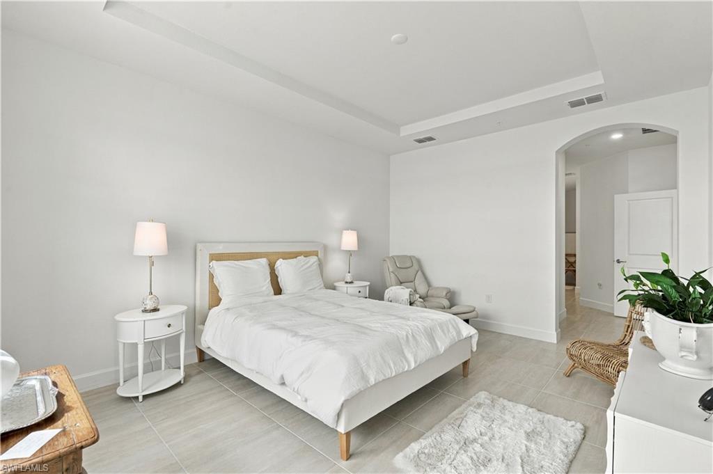 Furnished bedroom with a white bed, gray reclining chair, and arched doorway.