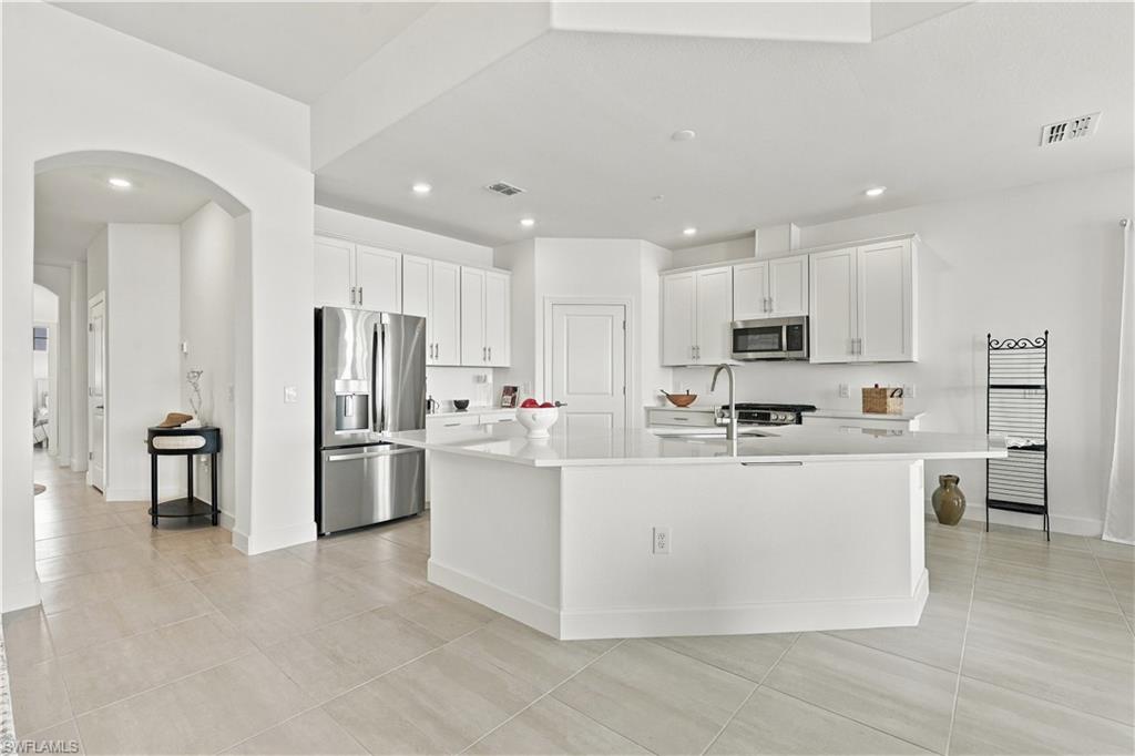 Bright white kitchen with a large island, stainless steel appliances, and pale tile floors.
