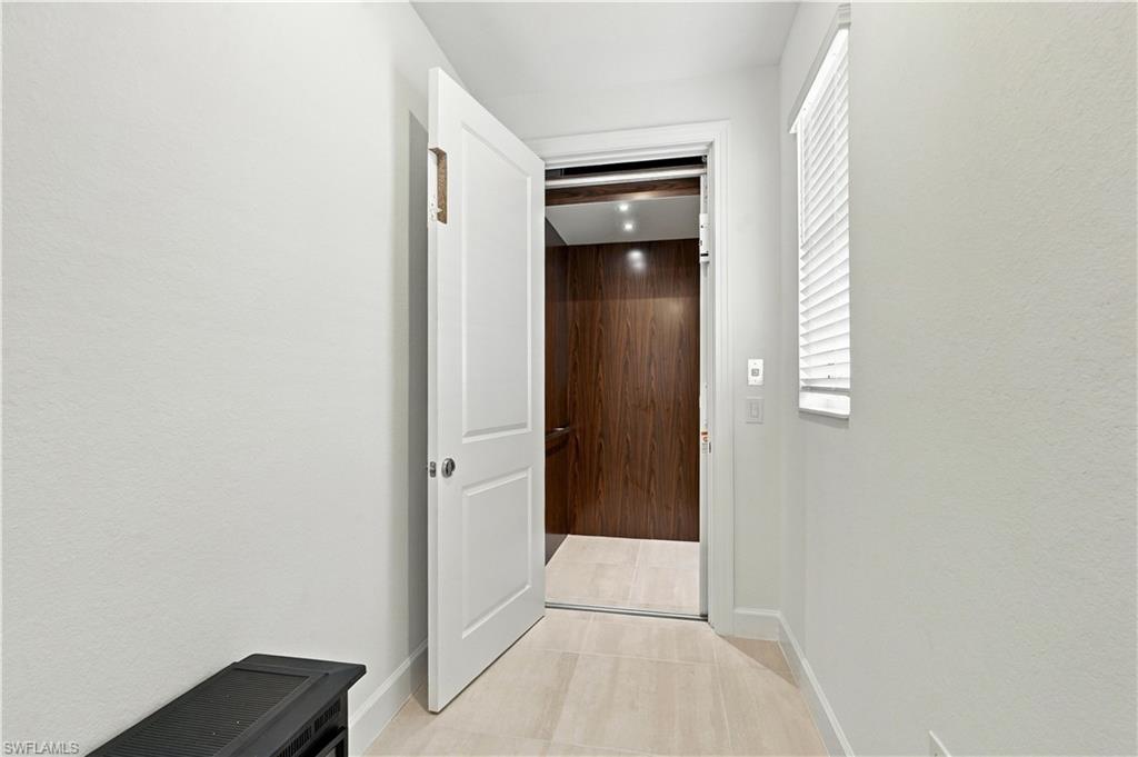 Bright tiled hallway opening to a wood-paneled elevator, with a window and white blinds.