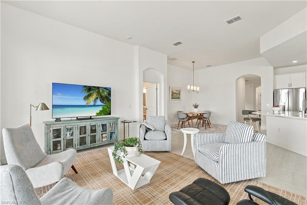 Open-plan living room with striped seating, a distressed green TV console, and adjoining dining area.