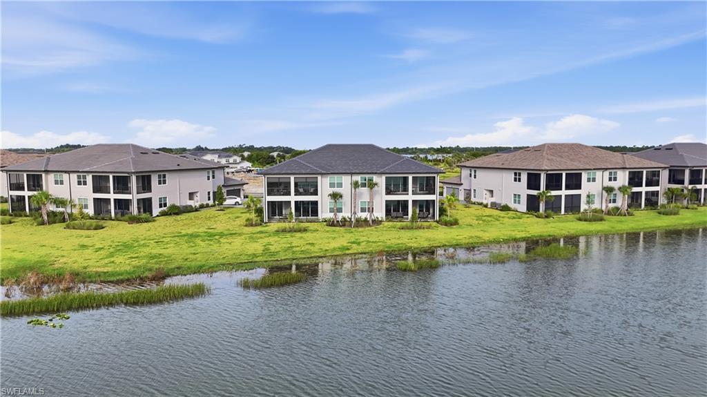 Two-story condominium buildings beside a canal, with grassy banks and neighboring homes.