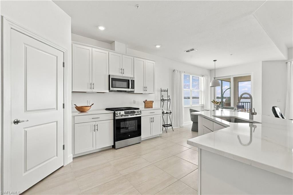 Bright white kitchen with a large island, stainless appliances, and water visible through the windows.