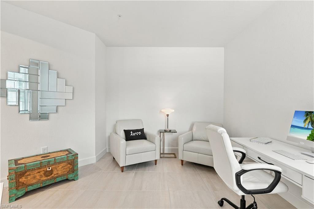 Home office with a white desk, two armchairs, geometric mirror, and colorful wooden chest.