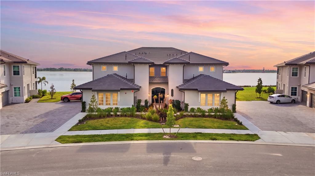 Two-story waterfront home with landscaped frontage and a sunset-lit lake behind it.
