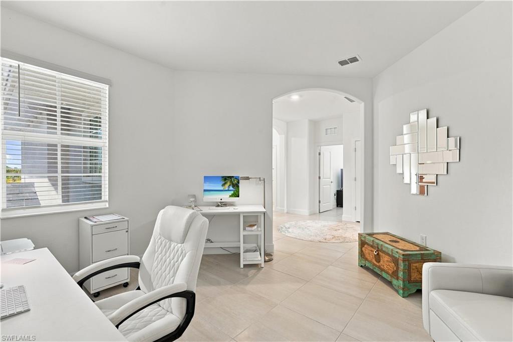 Bright home office with white desks, a quilted chair, and an arched opening to the hall.