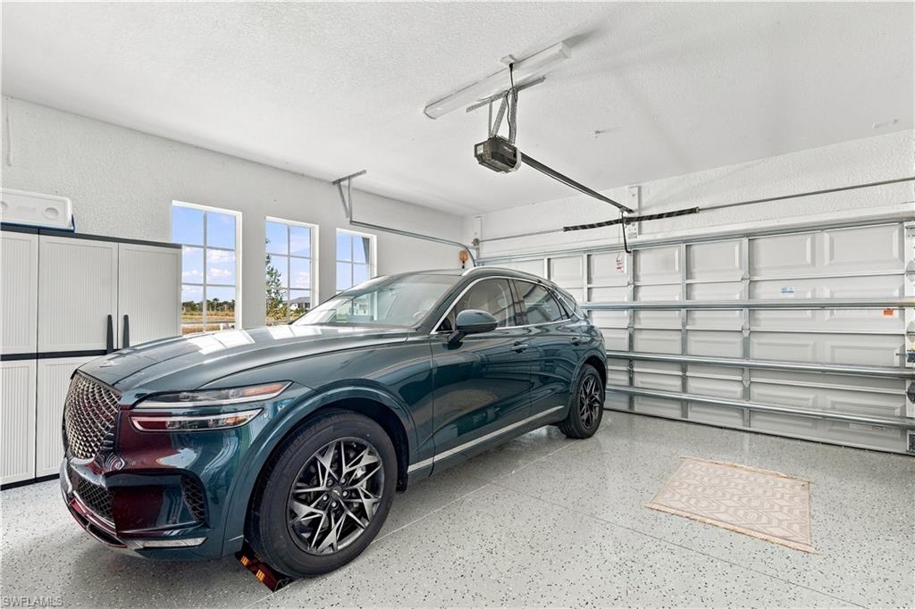 Garage with a dark teal SUV, white storage cabinets, tall windows, and a speckled floor.