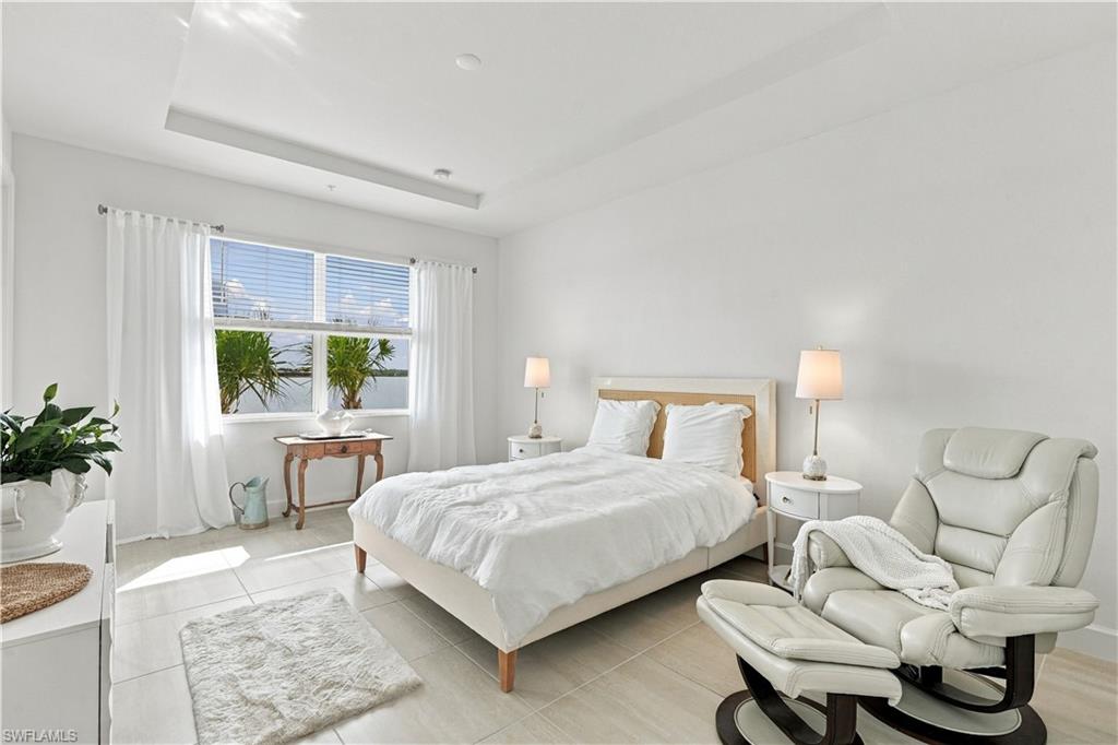 Bright bedroom with a white bed, curtained window, and cream recliner.