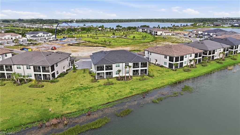 Aerial view of waterfront condominium buildings beside a lake, with green grounds and nearby construction.