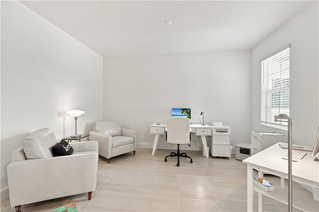 Home office with white desks, two armchairs, and a large window with blinds.