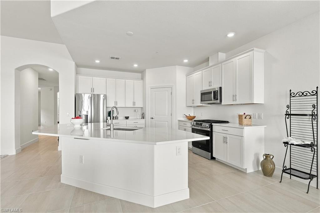 Bright white kitchen with a large quartz island, stainless steel appliances, and an arched doorway.
