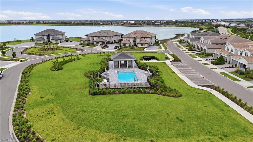 Aerial view of a community pool and pavilion on a landscaped lawn beside a lake.
