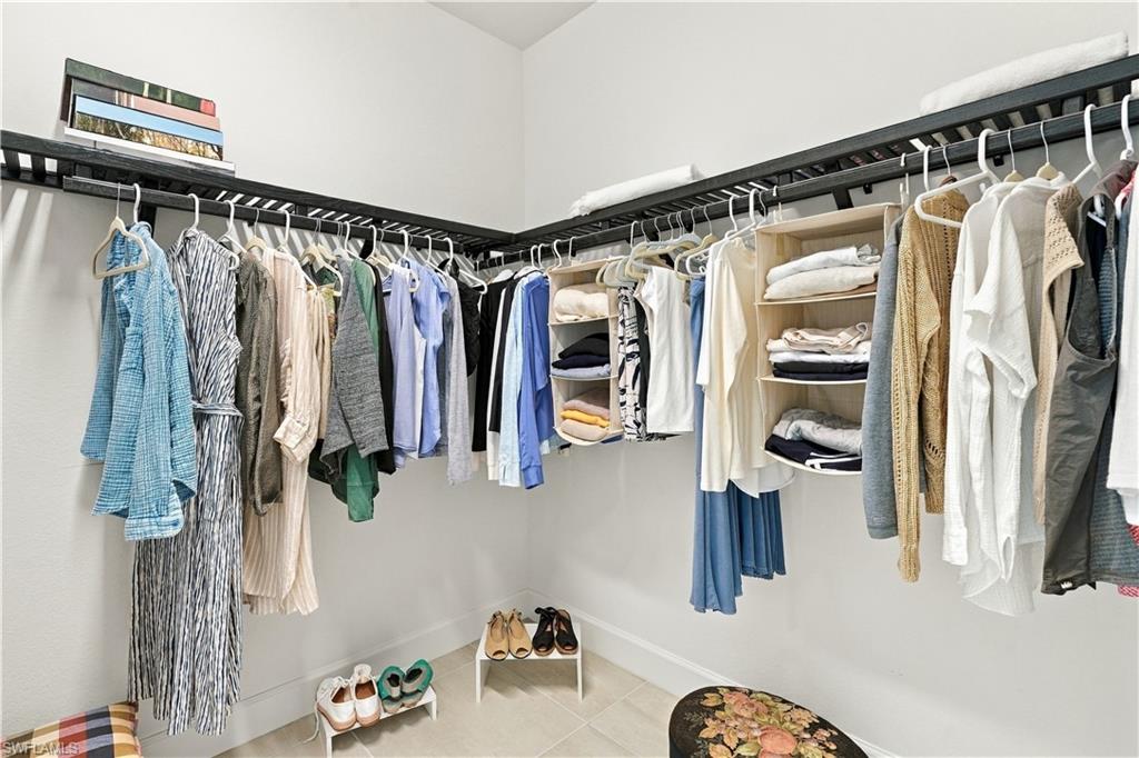 Walk-in closet with wraparound clothing rods, open shelves, and shoes arranged on the tiled floor.