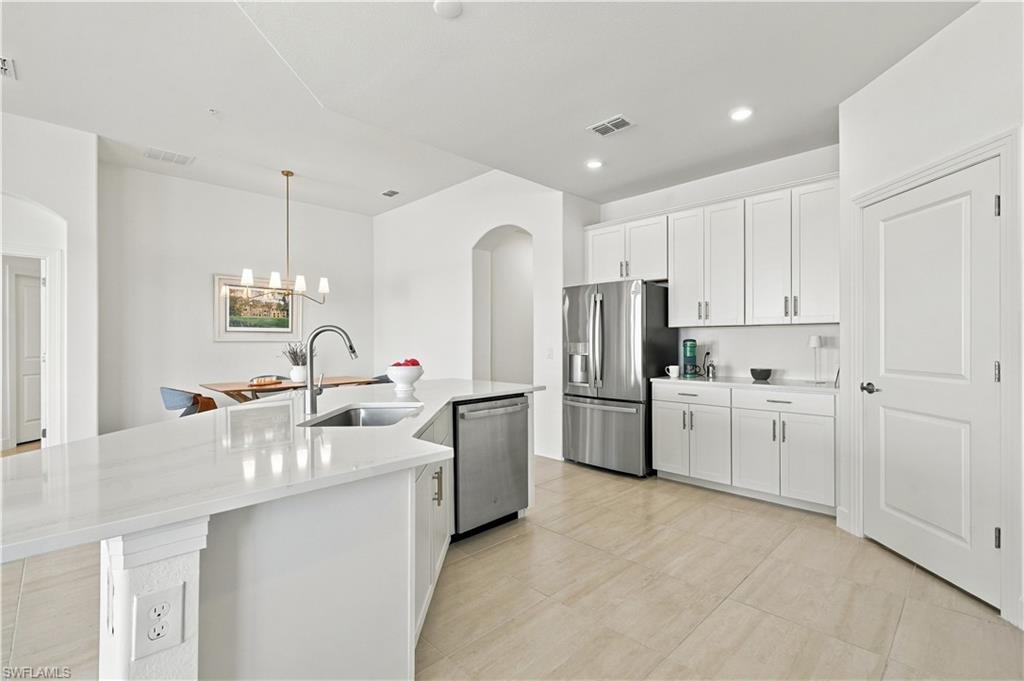 Modern white kitchen with a large quartz island, undermount sink, and stainless steel appliances.