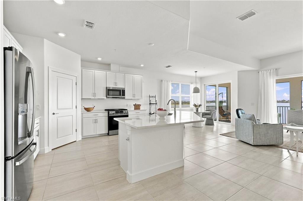Open kitchen with white cabinets, stainless appliances, and a large island beside a waterfront living area.