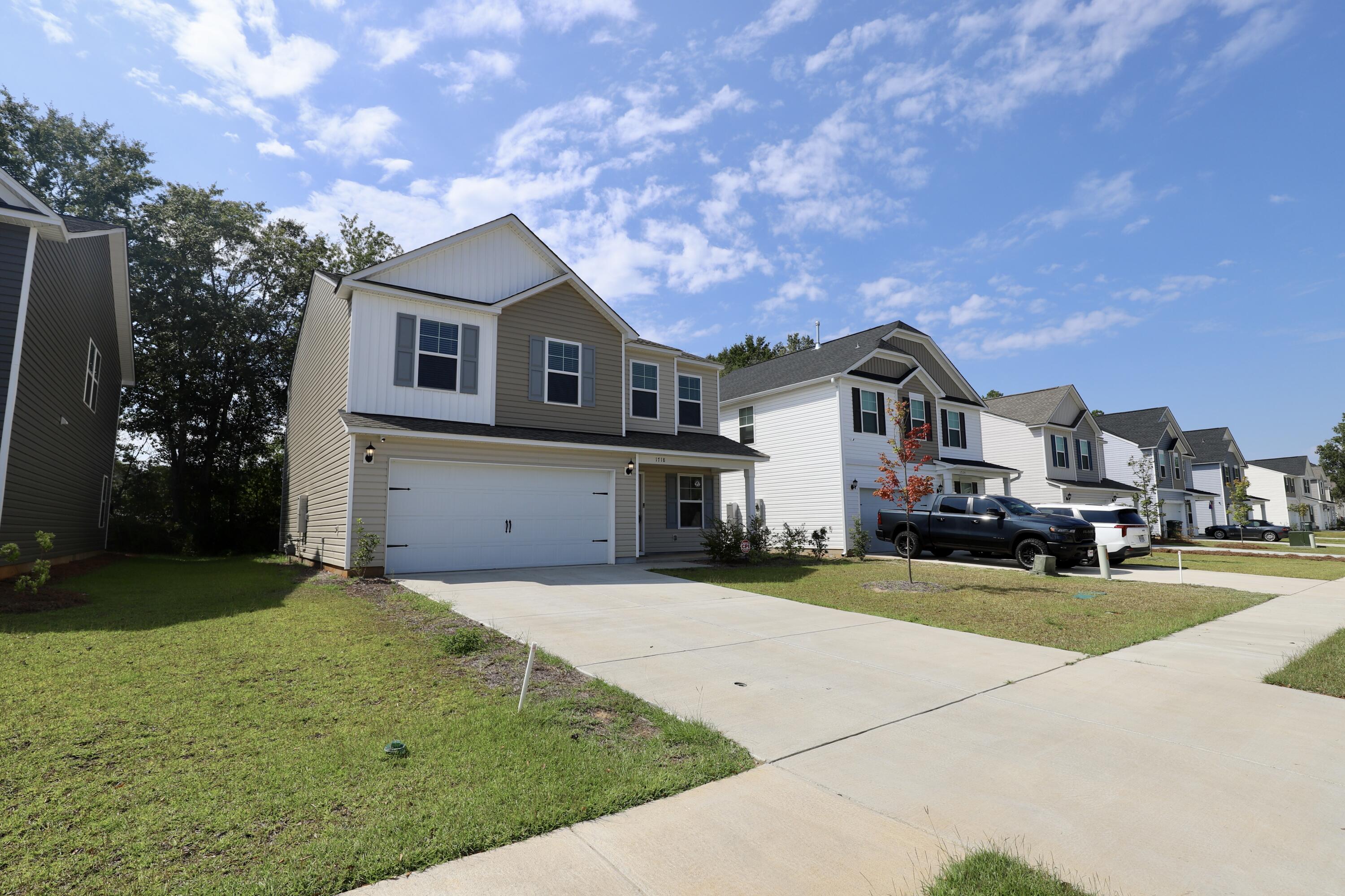 Two-story beige home with white trim, a double garage, and a wide concrete driveway.