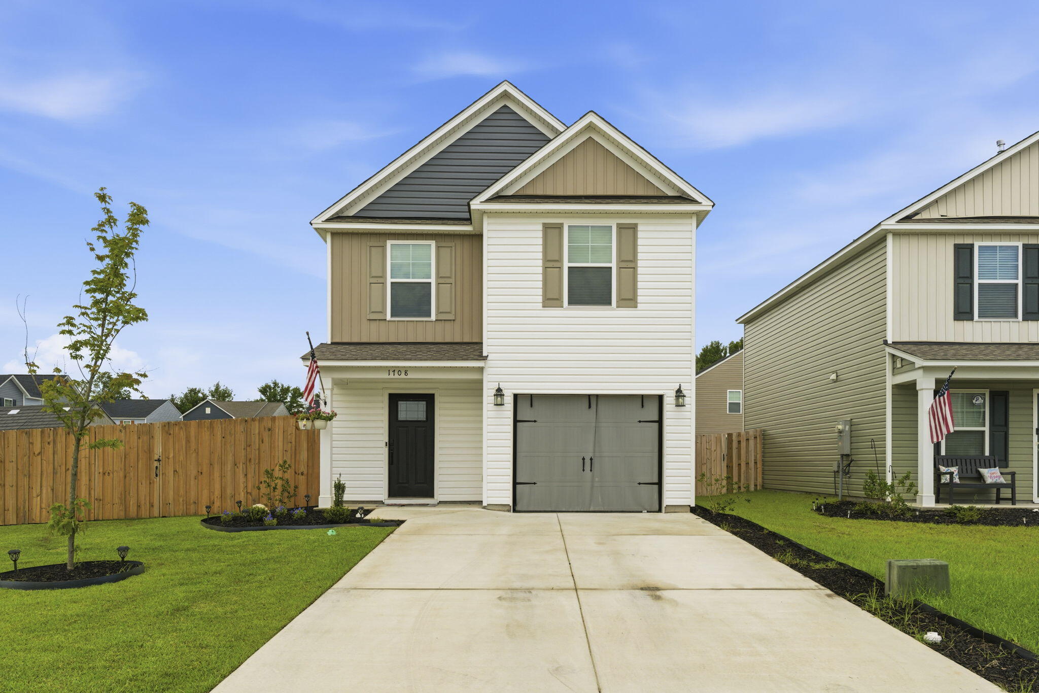 Two-story white and tan home with an attached garage, broad driveway, and fenced lawn.