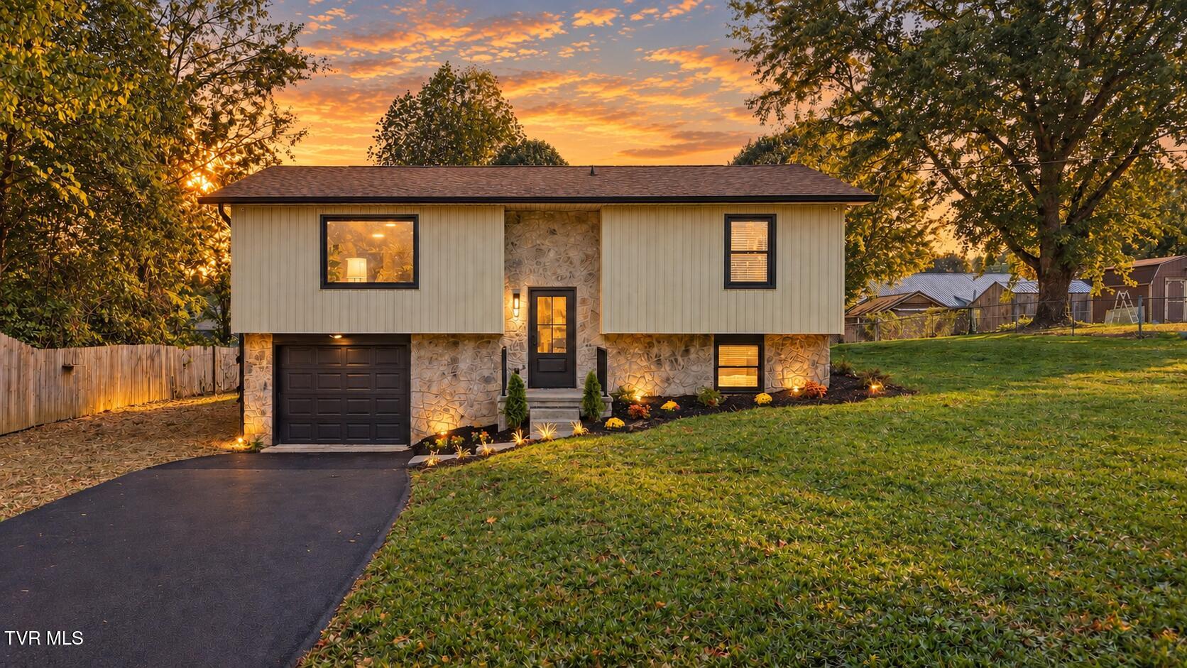 Split-level home with a stone facade and attached garage, warmly lit at dusk.