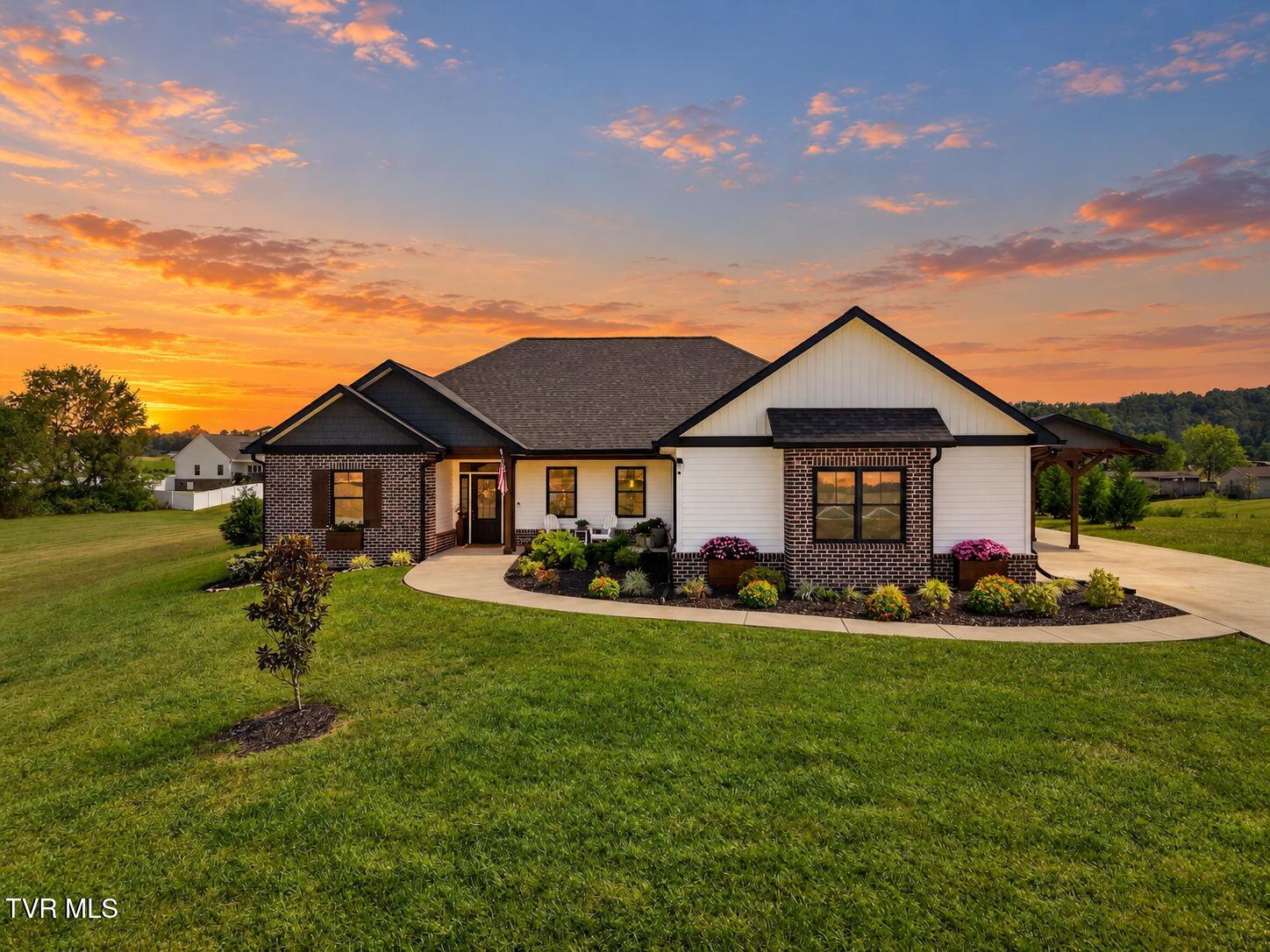 Single-story white-and-brick home with landscaped flower beds and a broad lawn at sunset.