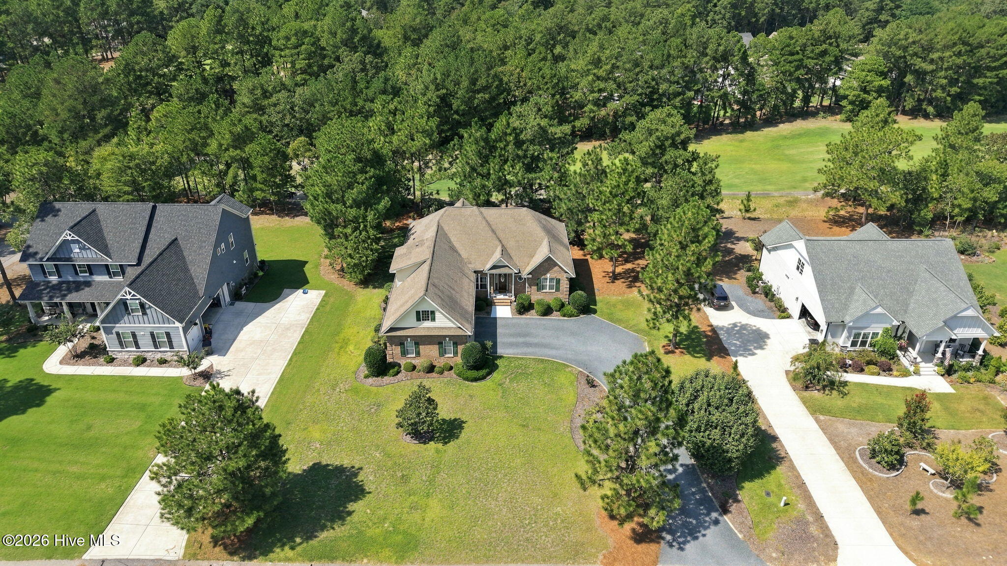 Aerial view of a brick home with a curved driveway, neighboring houses, and a grassy golf course area.