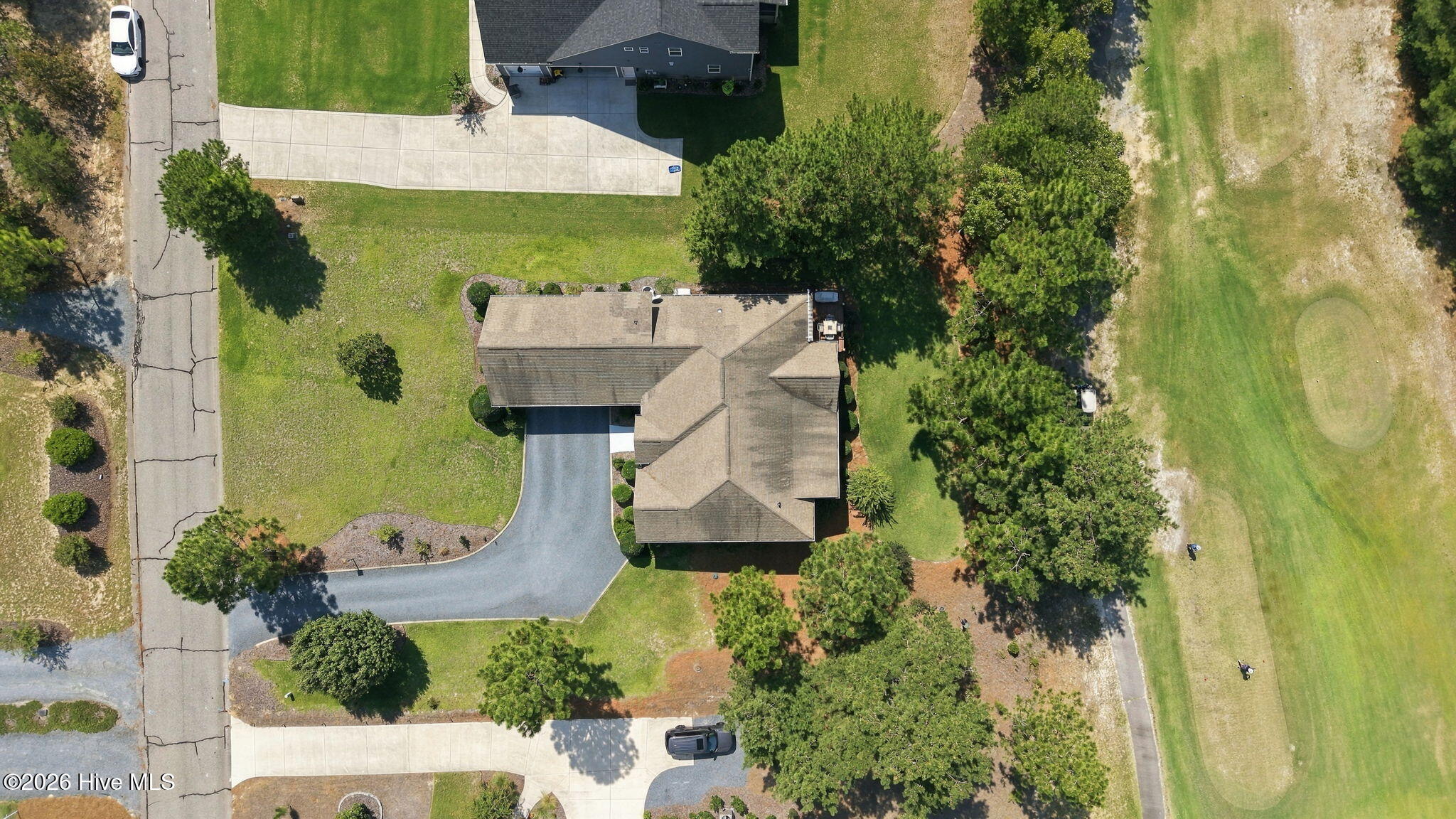 Aerial view of a home with a curved driveway and landscaped yard beside a golf course fairway.