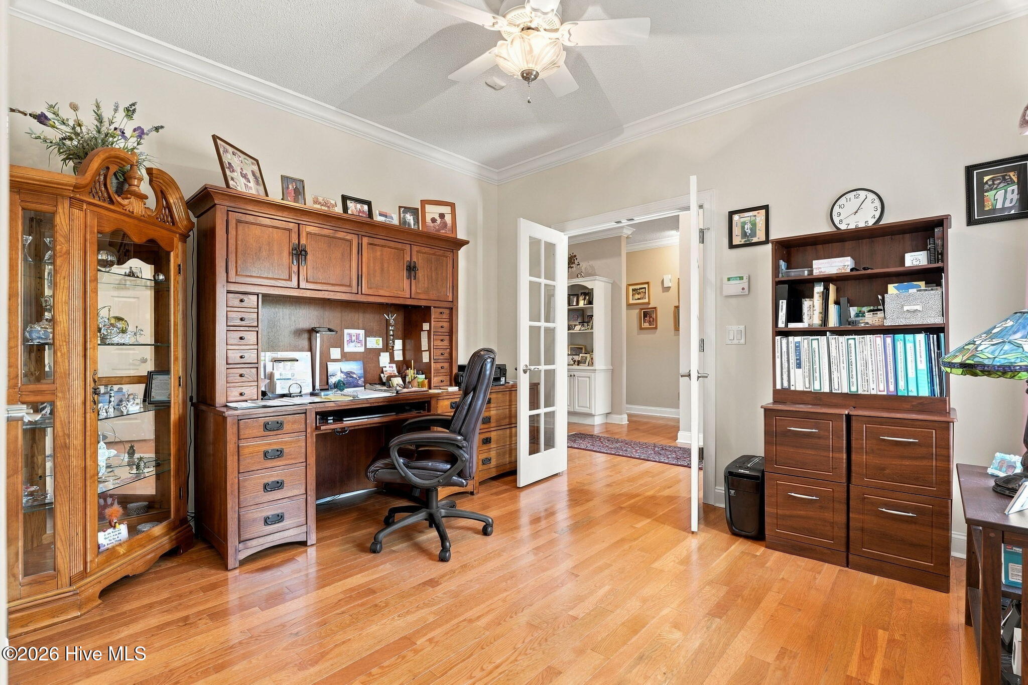 Home office with a large wooden desk, hardwood floors, and open French doors to the hallway.
