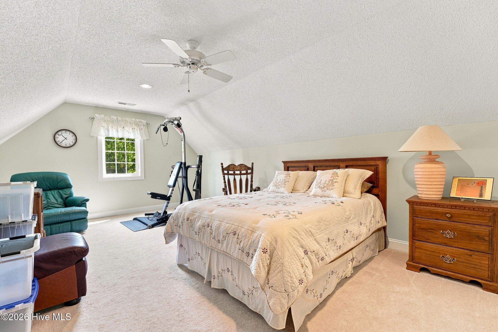Furnished bedroom with a sloped ceiling, wooden bed, and exercise equipment by the window.