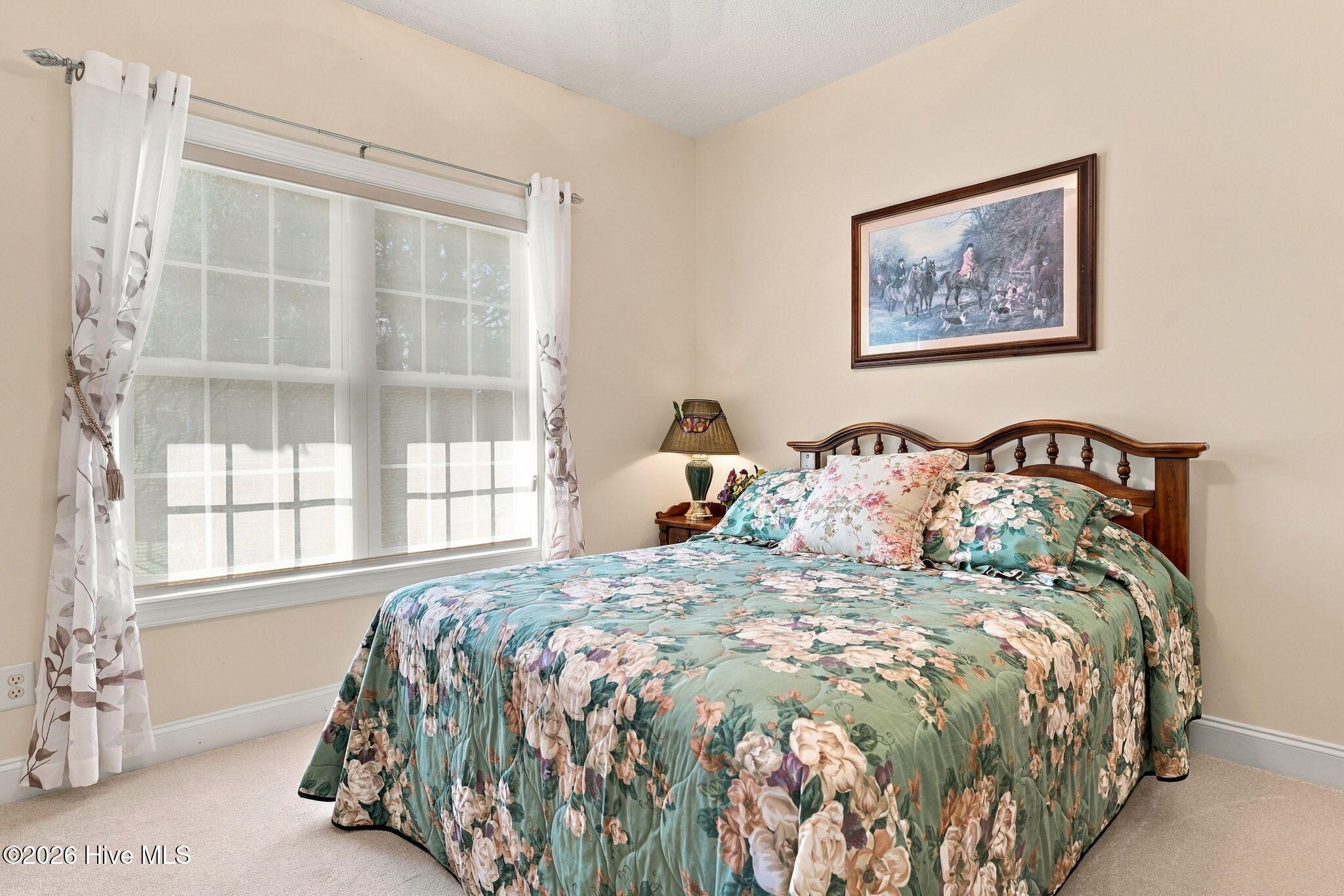 Bedroom with teal floral bedding, a wooden headboard, and a large curtained window.