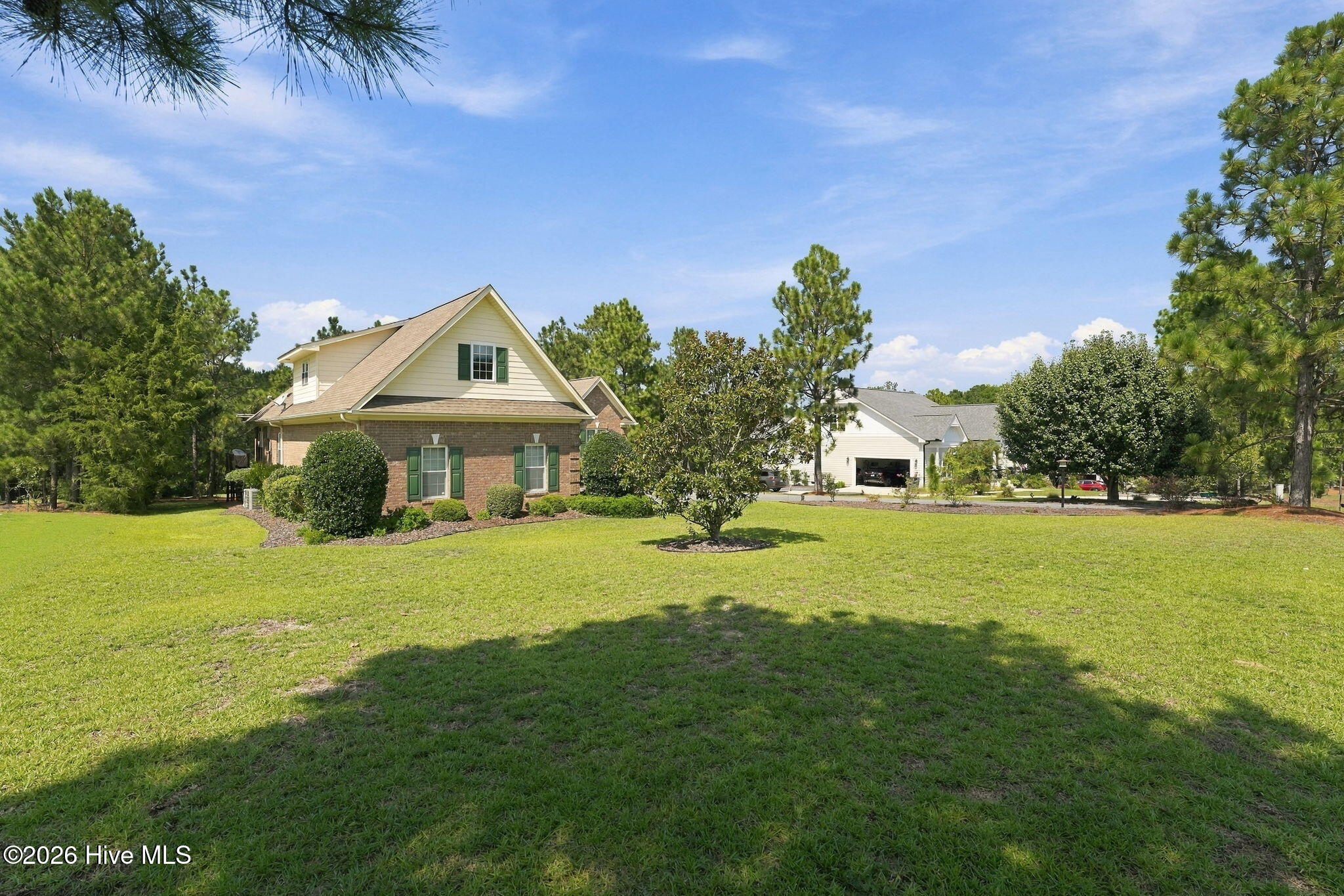 Two-story brick and siding home with green shutters, a broad lawn, and mature pine trees.