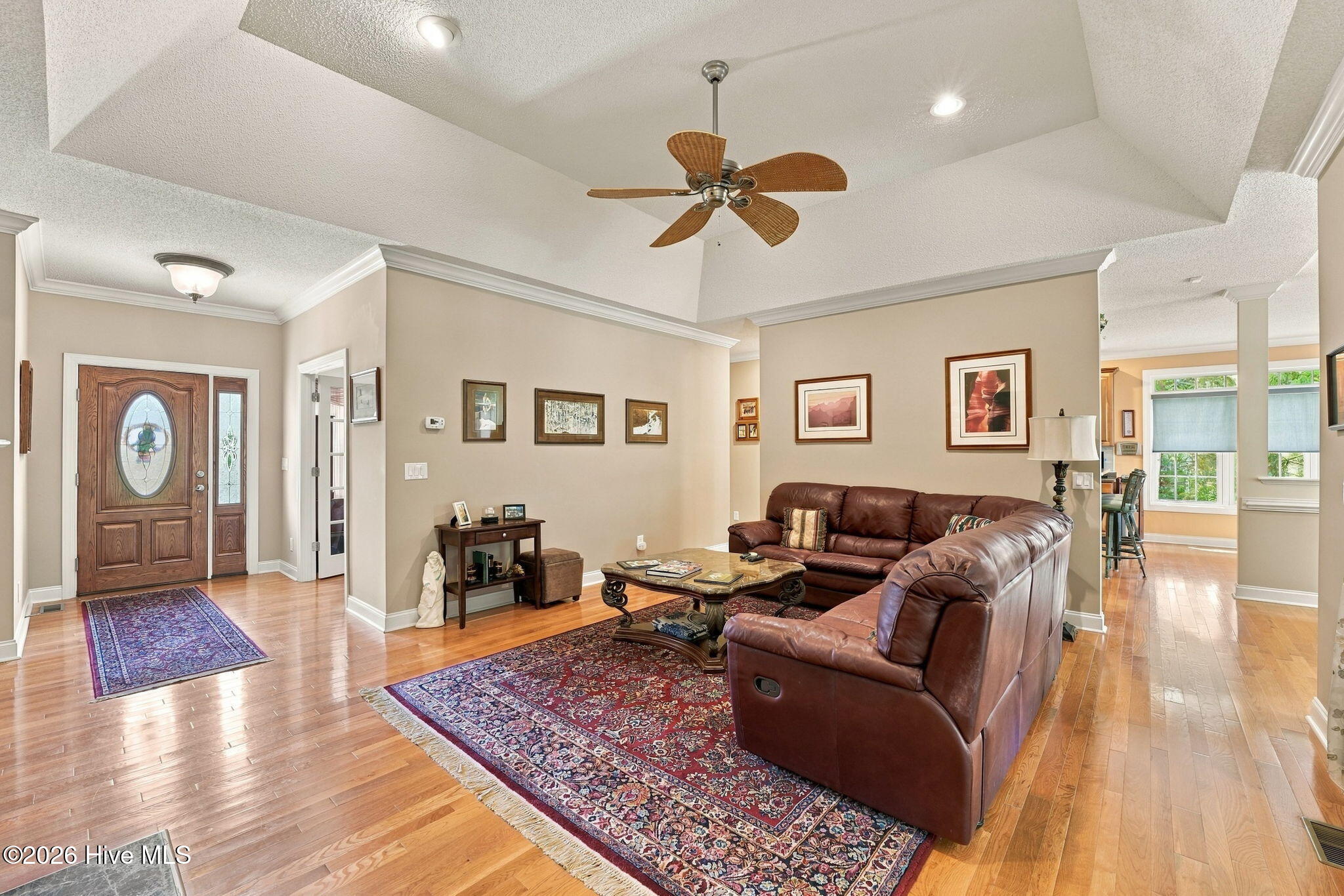 Living room with a brown leather sectional, patterned rugs, and an entryway with a decorative-glass front door.